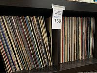 Shelf with two dozen plus vinyl LP records in cardboard sleeves, full lot overview