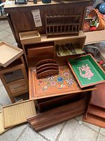 Various wooden trays and cigar cases stacked and arranged on floor including colorful floral and green graphic trays, wooden letter holder, and display rack