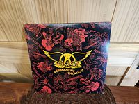Front cover of the LP album showing black background with red and yellow graphic design and Aerosmith Permanent Vacation logo.