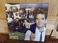Front cover of Huey Lewis and The News Sports album showing band members in a bar with pool table and the title logo