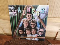 Front cover of Madness 1983 Canadian Geffin Records album showing six band members arranged on green stairs with colorful lettered band name 'MADNESS' and billiard balls.