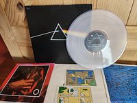 Gatefold cover, clear vinyl LP laid atop, red bordered poster, two stickers and blue poster beneath