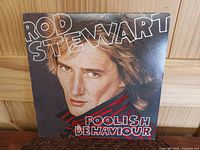 Front cover of Rod Stewart 'Foolish Behaviour' vinyl album featuring close portrait of Rod Stewart with bold white and red text.