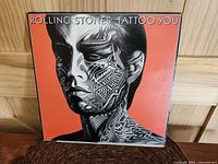 Front cover of the Album showing the stylized tattooed face on orange background.