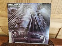 Front cover of Steely Dan - The Royal Scam vinyl LP showing surreal art of man sleeping surrounded by statues and pillars.