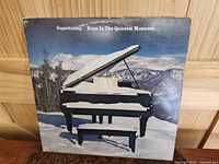 Front cover of Supertramp 'Even In The Quietest Moments' LP showing a grand piano in snow with mountain background and visible corner and edge wear.