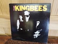 Front cover of 'The Kingbees' album with black background and yellow/pink band name text, showing edge wear and corner stress creases.