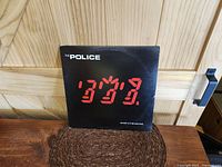 Front cover of The Police vinyl LP Ghost In The Machine. Black background with red stylized text. Shows some corner and edge wear.