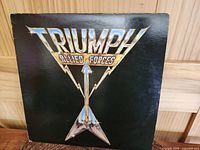Front cover of Triumph Allied Forces 1981 vinyl album showing metallic guitar logo on black background.