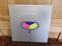Front cover of Yes 90125 album showing geometric colorful design with 'YES' text on silver background.