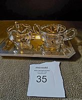 Glass cream and sugar set with floral detail and '1000 Islands' engraving on small metal tray.