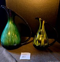 Both vintage Blue Mountain Pottery pitchers showing distinct blue-green and rare green flow glaze colors, with dark brown-black handles and spouts, placed side by side.
