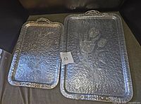 Photo showing both vintage hammered aluminum serving trays with tulip designs, placed side by side.