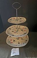 Front view of the assembled 3-tier cake plate showing all three porcelain plates and metal support rod with handle.