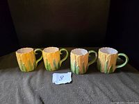 Four corn-shaped ceramic mugs shown front view on dark fabric background