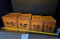 Four wooden rooster canisters lined up with tape measure for size reference.
