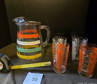 Full set showing large glass pitcher with colored stripes alongside six colorful patterned glasses on black background.