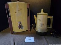 Photo showing the green vintage coffee urn with spigot and a matching coffee percolator side by side on a cloth surface, cords visible.