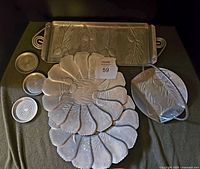 7 pieces of hammered aluminium serveware laid out on a dark surface including 3 coasters, 2 round trays, 1 rectangular tray with handles, 2 basket trays featuring a pinecone and foliage design.
