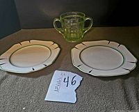 Photo shows the green depression glass spooner with ribbed design and two handles, centered behind two white Adams china plates with art deco edge and green rim accents.
