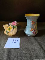 Two vintage pottery pieces: a cream-colored James Kent Longton pitcher with floral and fruit motifs and a green handle, and a blue Radnor flower vase with berries and flowers decoration.