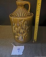 Front and side view of the vintage McCoy avocado green cookie jar showing embossed text 'Cookies Joe' and ribbed lid with handle, next to a ruler showing approx 11.5 inches tall.