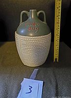 Front view of ceramic McCoy Cookie Jug cookie jar with tape measure showing height approximately 10 inches, soft green base with rope design texture, and red 'Cookie Jug' lettering.