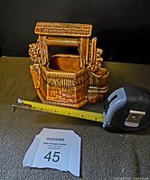 Clear front and side views of the brown ceramic wishing well planter with embossed 'Wishing Well' lettering, attached metal chain, and detailed brick pattern design.
