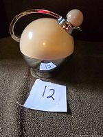 Front and side view of spherical glass vacuum bottle with cream top and chrome bottom, curved chrome handle and spherical cream stopper, placed on dark textile surface.