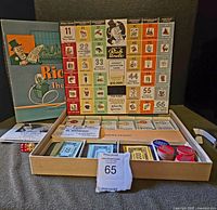 Complete stock market game set displayed with open wooden case organizer showing dice, play money, chips, and market cards. Vertical game board with numbered boxes is visible.