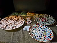 Wide view showing assortment of six mosaic tile pieces including large plates and console bowl with varied colors and patterns