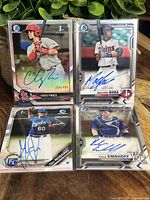 Four autographed Bowman Chrome baseball cards in plastic protective sleeves, including Chase Pinder refractor numbered 254/499 and three other player autographs.