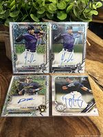 Four signed Bowman Chrome baseball cards displayed on a wooden surface with green leaves in the background; two cards of Helcris Olivarez and one Pablo Abreu short print numbered 072/299 with holographic sparkle finish and autograph.