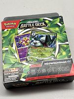 Front of the sealed Pokémon Deluxe Battle Deck box showing holographic Meowscarada EX and Radiant Alcremie cards on the packaging with green leaf background.