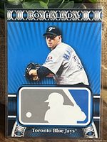 Front of Roy Halladay 2010 Topps MLB Logoman card showing Halladay pitching with large MLB batter silhouette logo and Toronto Blue Jays identification.