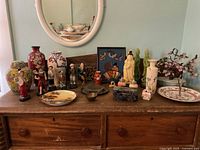 Wide shot of table showing assorted Asian inspired figurines, vases, plates, and decorator items excluding mirror.