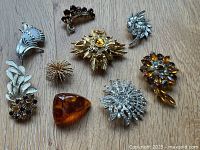 Top view of nine assorted vintage brooches showcasing various styles, colors, and materials on a wood background.