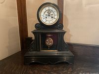 Front view of the antique marble base mantel clock showing the round clock face with Roman numerals and visible winding keyholes.