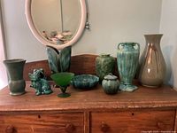 Full view of set of seven pottery and glass items on wooden surface with mirror behind