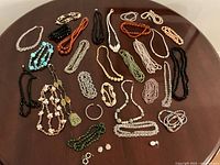 Overhead photo showing a large assortment of beaded necklaces, bracelets, earrings and pendants of various colors laid out on a brown surface.