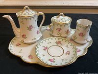 Front angle showing the full setup of tea service on serving tray including teapot, sugar bowl, creamer, and saucer with floral and gold detail.