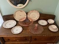 Photo showing entire collection on wooden surface including floral china plates, cups, and pink glass pieces.