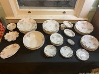 Overview of an assortment of porcelain dishware including plates, bowls, and small dishes with floral designs and gold trim.
