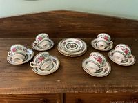 Six Paragon teacups each paired with a saucer arranged around five dessert/salad plates on a wooden surface.