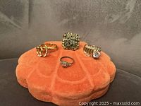 Four rings displayed on orange velvet shell-shaped cushion, showing details and condition of each ring