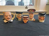 Five character ceramic toby jugs on black cloth showing various detailed faces including a soldier and theatrical figures