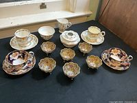 Collection of tea cups, saucers, decorative small bowls, and covered dish arranged on a wooden surface near window.