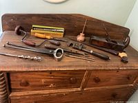Overall view of the vintage hand tools arranged on wooden furniture, showing the brace drill, augers, oil can, pipe wrench, hand plane, saw, and mallet