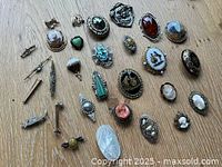 Group shot showing all 24 brooches and pins laid out on wood surface