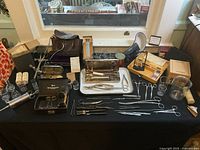 Full overview of table with leather bag, instrument cases, stainless steel tools, glassware and charts